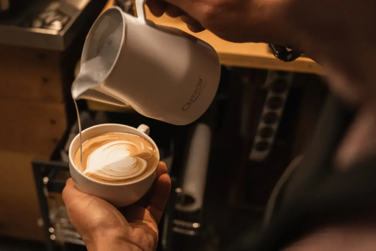 Barista verziert einen Kaffee mit kunstvoller cafe latte art. Ein Herz aus Milchschaum entsteht.