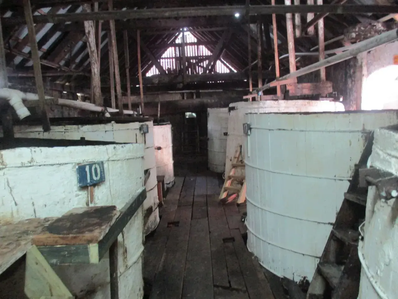Große weiße Bottiche in einer alten Lagerhalle, vielleicht zur Herstellung von Rum-Inhaltsstoffen.