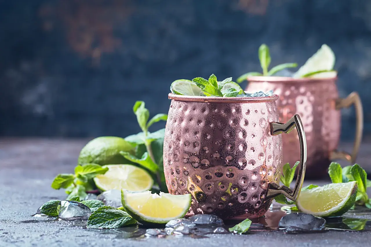 Zwei eisgekühlte Moscow Mule Becher mit Limette und Minze. Die Herkunft des Moscow Mule ist eine interessante Geschichte.