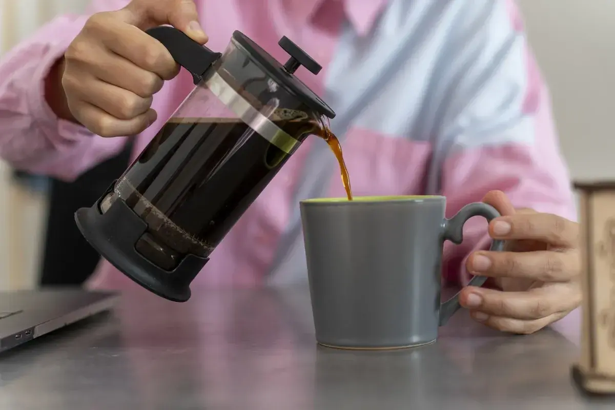 Kaffee wird aus einer French Press in eine graue Tasse gegossen.