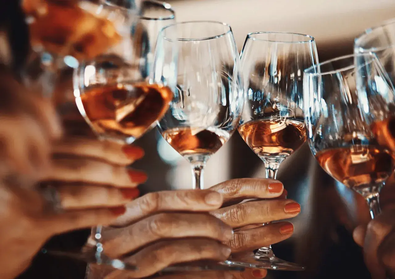 Hände halten Gläser mit Roséwein. Die Frage, warum Sulfite im Wein sind, beschäftigt viele Genießer.