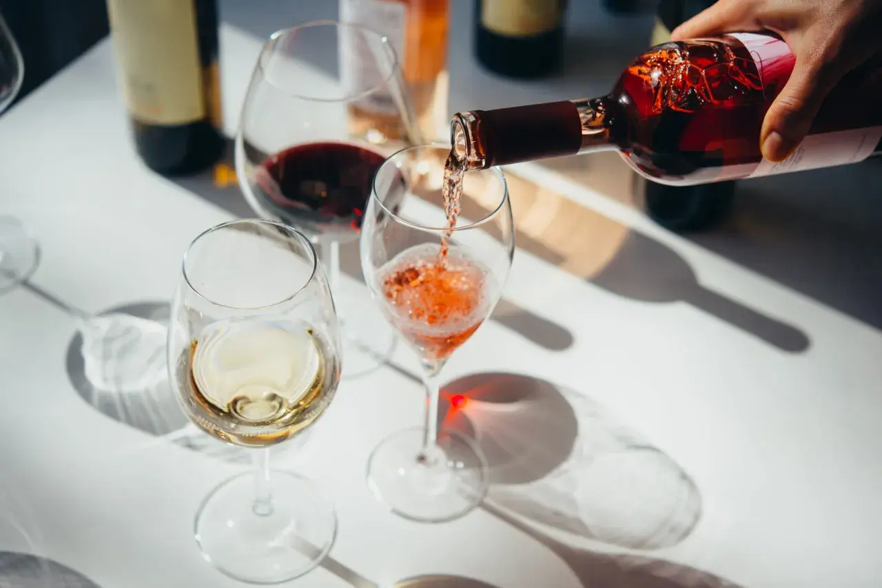 Roséwein wird in ein Glas gegossen, während Weiß- und Rotwein bereits in anderen Gläsern stehen. Ein schöner Moment, um Wein zu servieren.