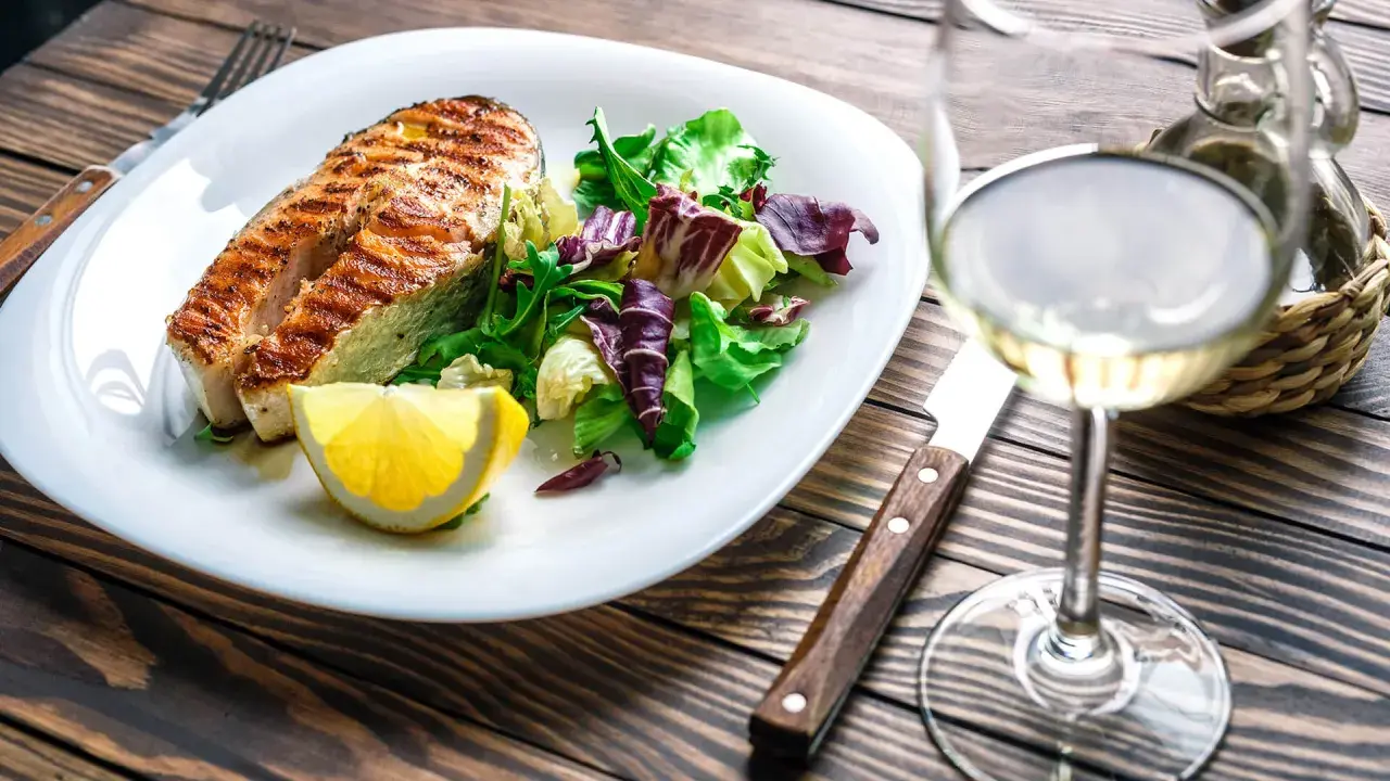 Gegrilltes Lachsfilet mit Salat und Zitrone, dazu ein Glas Weißwein, der den Riesling Geschmack unterstreicht.
