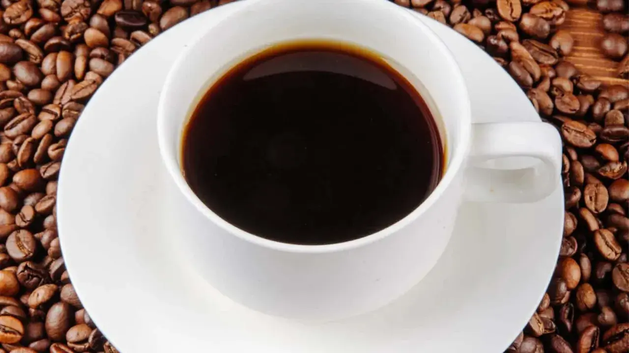 Eine Tasse schwarzer Kaffee umgeben von gerösteten Kaffeebohnen. Die Frage "wie viel Koffein hat Kaffee?" wird durch dieses Bild aufgeworfen.
