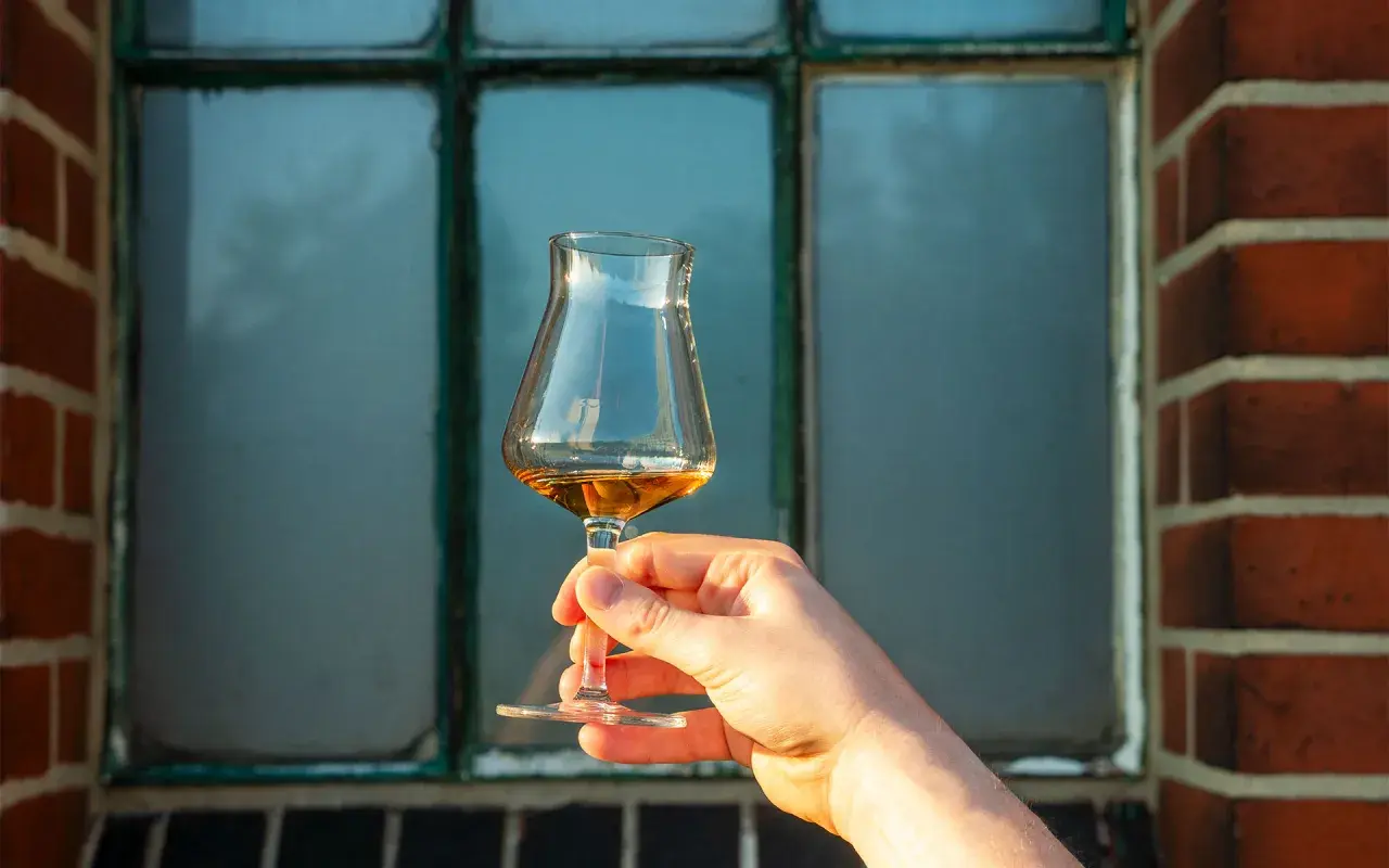 Hand hält ein Glas mit bernsteinfarbenem Whisky. Der Alkoholgehalt des Whiskys wird durch die Farbe und Klarheit angedeutet.
