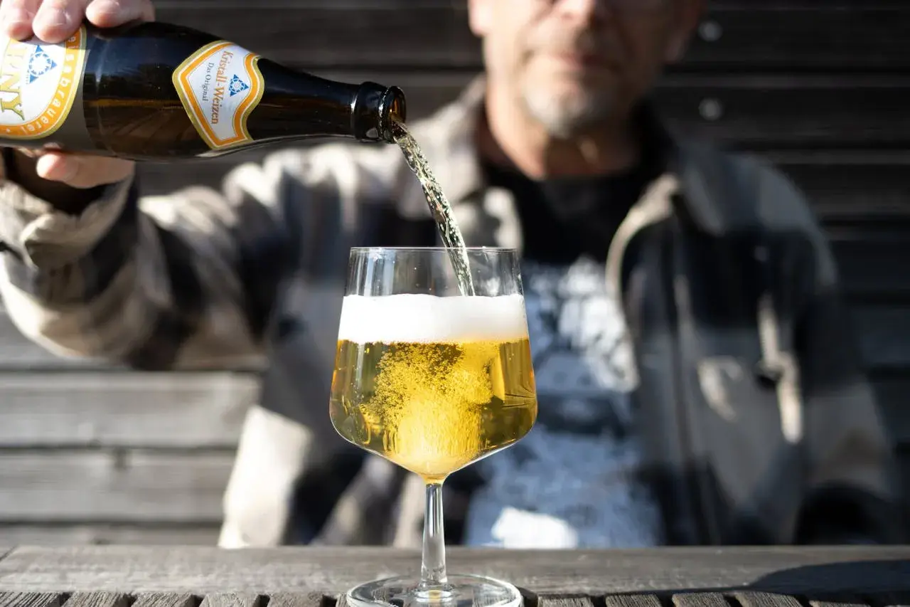 Ein Mann gießt ein Kristall-Weizenbier in ein Glas. Die Flasche zeigt "0,33l". Wenige Kalorien für diesen Genuss.