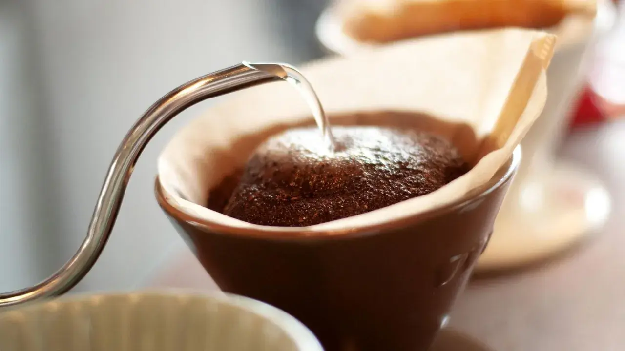 Heißes Wasser fließt aus einer schmalen Kanne auf frisch gemahlenen Kaffee in einem Filter. Der Prozess des Kaffee filterns beginnt.