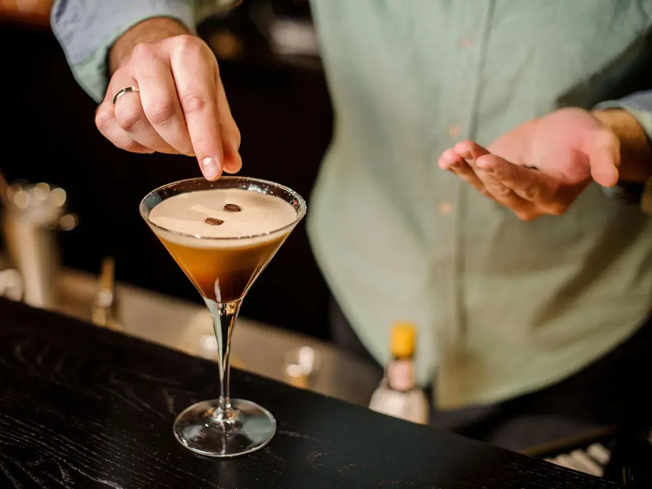 Ein Barkeeper garniert einen Espresso-Martini mit Kaffeebohnen. Dieser Kaffee Cocktail ist ein Genuss.