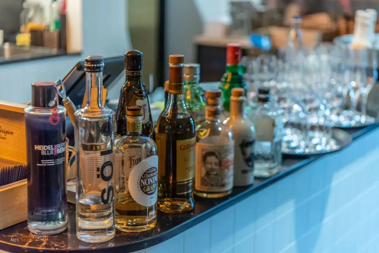 Eine Auswahl an Flaschen, darunter eine blaue Heidelbeer-Wodka-Flasche, steht auf einer Bar. Was ist Wodka? Eine klare Spirituose, oft aus Getreide oder Kartoffeln hergestellt.