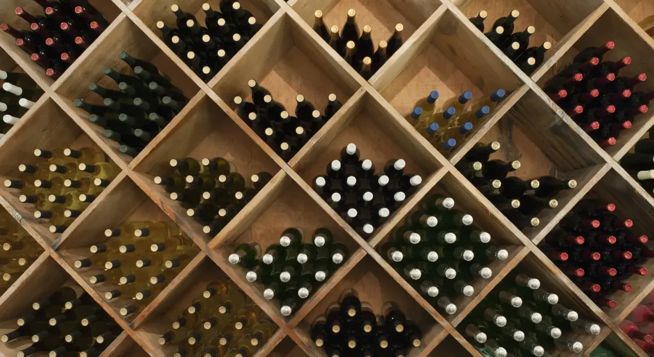 Holzregal mit vielen Flaschen Wein, ideal zum rotwein lagern. Verschiedene Sorten und Farben sind zu sehen.