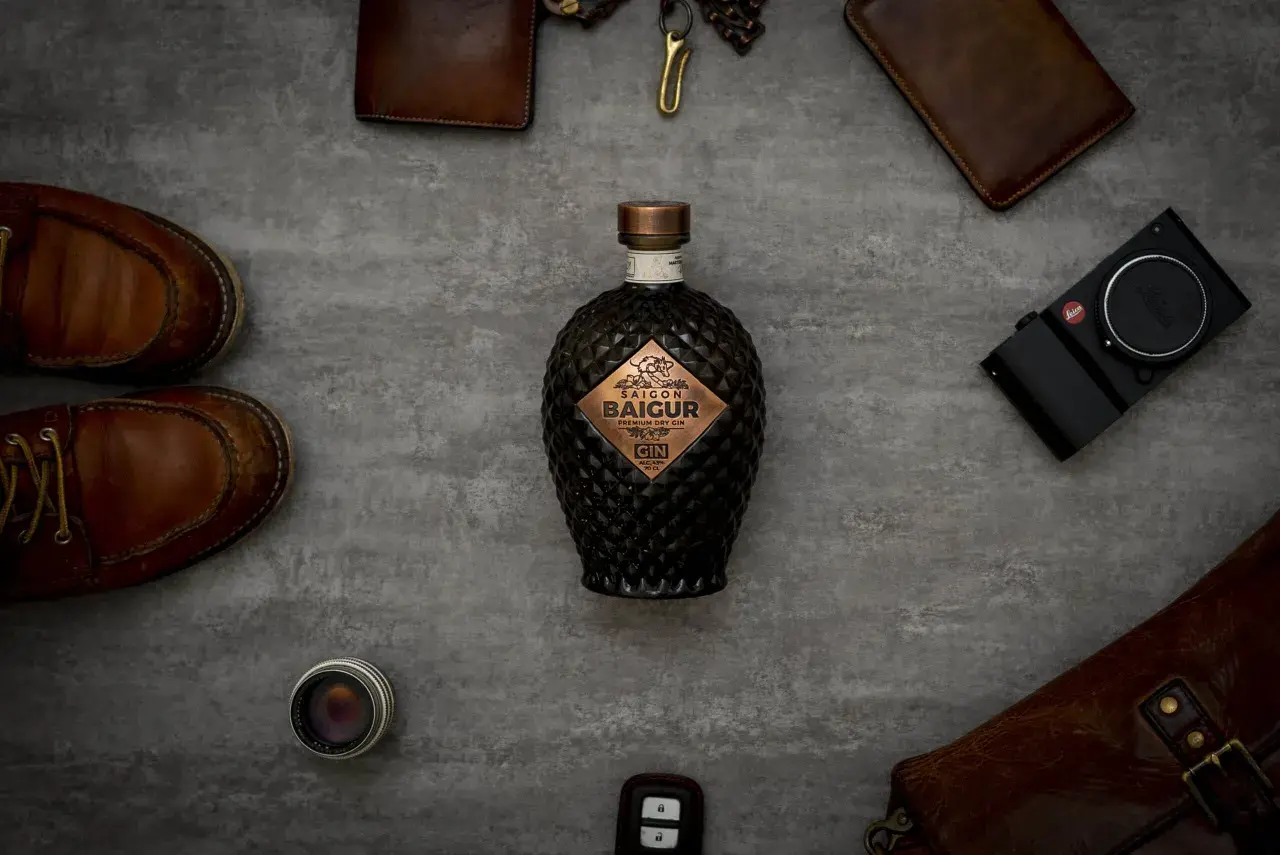 Edle Flasche Saigon Baigur Gin mit 43% Alkohol, umgeben von Lederaccessoires und einer Leica Kamera.