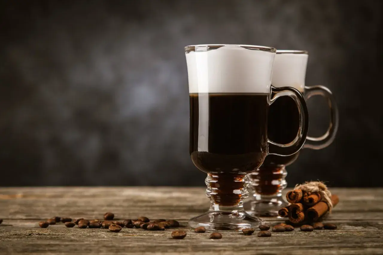 Zwei Irish Coffee Gläser mit Sahnehaube, Kaffeebohnen und Zimtstangen. Perfekt für Irish Coffee Rezepte.
