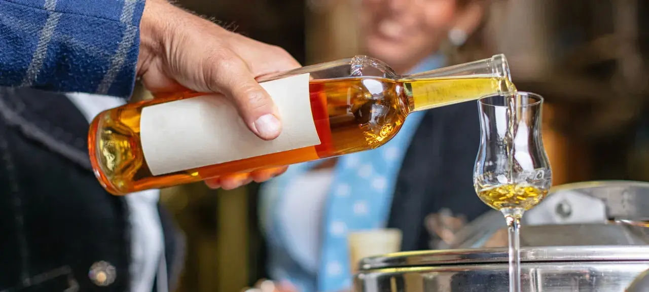 Ein Mann gießt goldbraunen Grappa in ein Glas. So trinkt man Grappa kalt, ein Genuss für besondere Momente.
