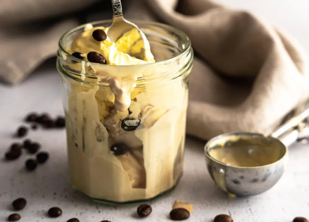 Cremiges Kaffee-Eis im Glas, perfekt für ein schnelles Rezept. Ein Löffel hebt das köstliche Eis hervor, umgeben von Kaffeebohnen.