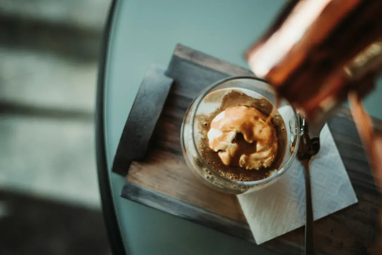 Ein Affogato: heißer Espresso fließt über eine Kugel cremiges cafe eis. Ein Löffel liegt daneben.