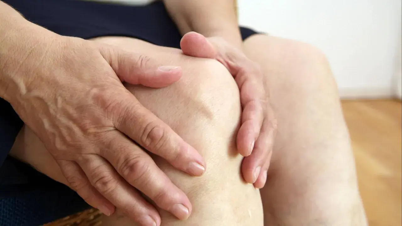 Hände umfassen ein schmerzendes Knie. Mögliche Ursache: Sulfite im Wein können Gelenkschmerzen verstärken.
