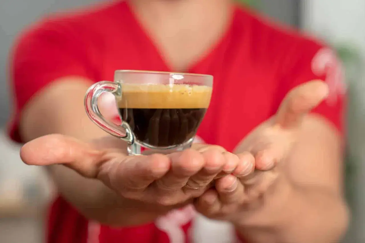 Hände reichen eine kleine Tasse Espresso, bereit für einen belebenden Kaffee-Nap.