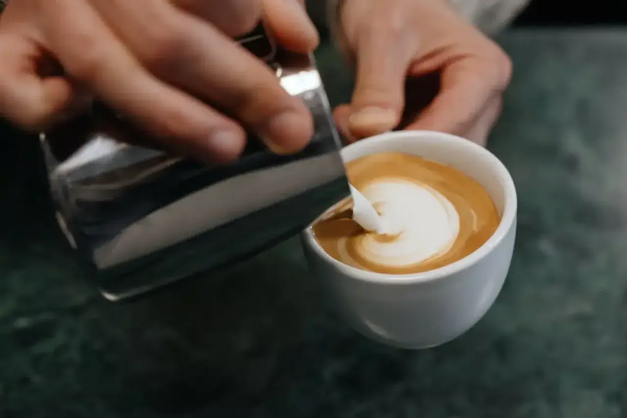 Barista zaubert mit Milch und Espresso ein Herz in die Tasse – ein Meisterwerk der Barista Art.