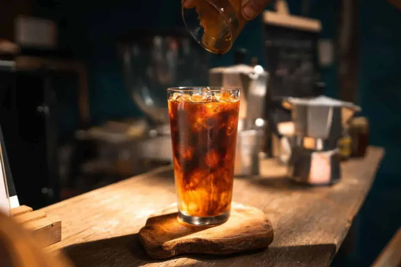 Ein erfrischender Eis Americano wird zubereitet, während Espresso in das Glas mit Eis und Wasser gegossen wird.