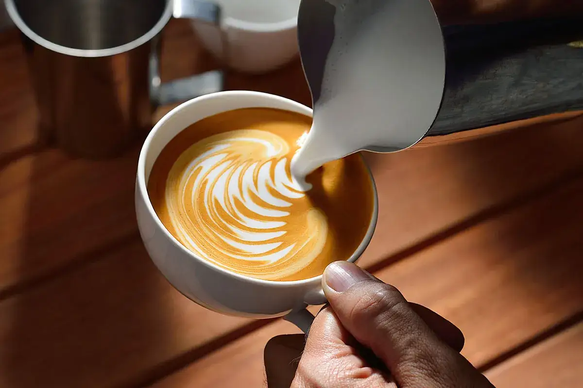 Barista gießt Milchschaum mit feinem Fettgehalt in eine Tasse Kaffee, um ein Latte Art Muster zu kreieren.