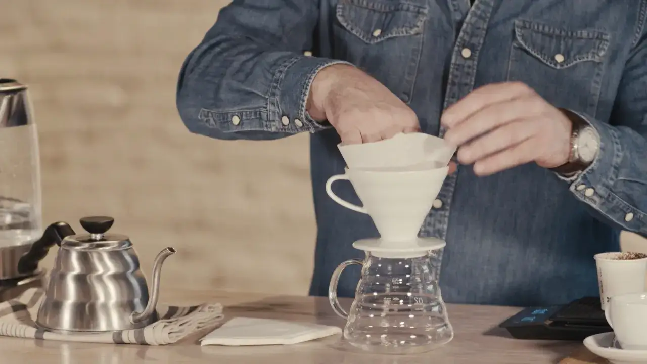 Mann bereitet sich darauf vor, Kaffee zu kochen, indem er einen Papierfilter in einen Porzellanfilterhalter legt.