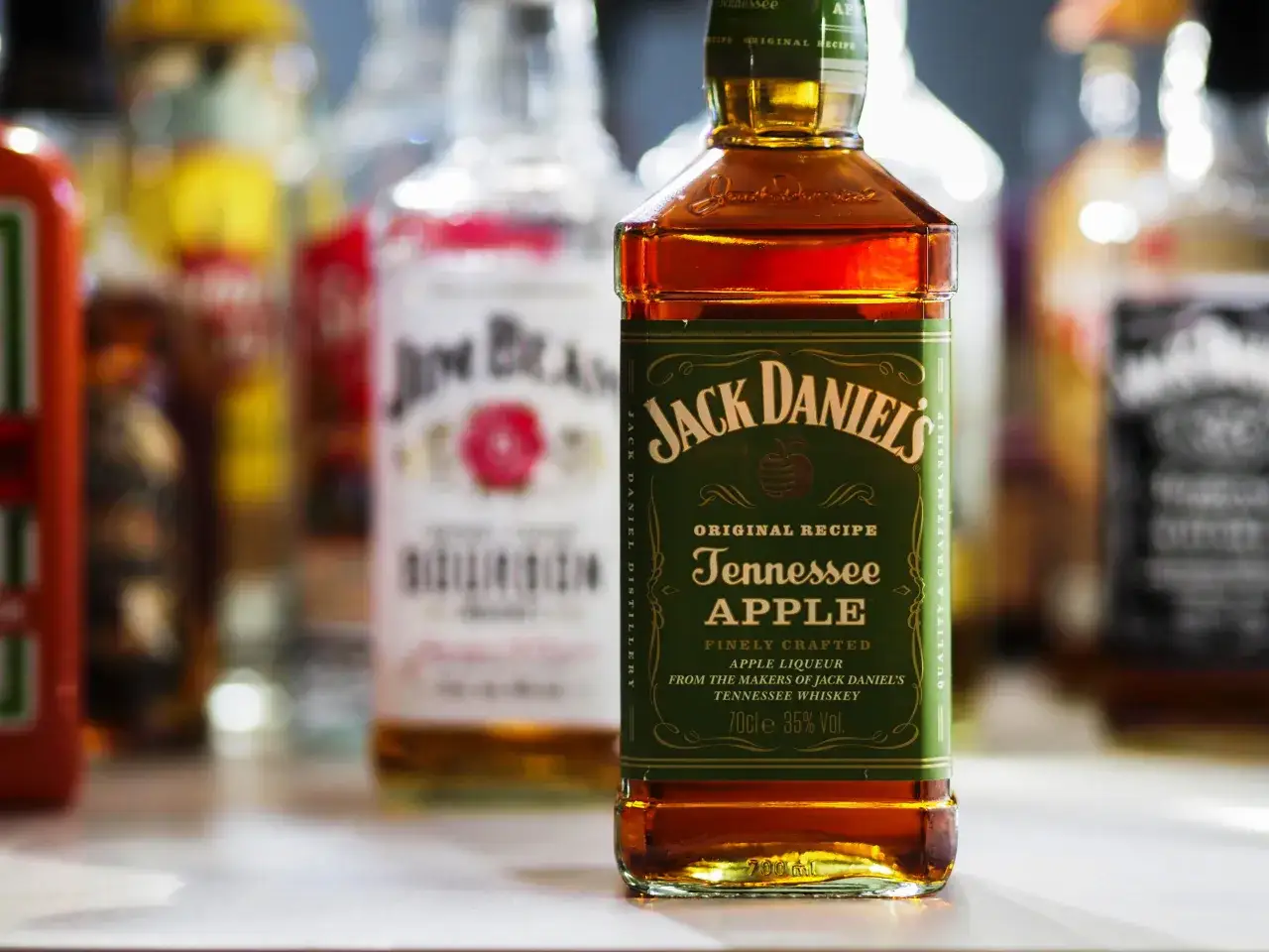 Jack Daniel's Tennessee Apple Likör mit 35% Vol. Alkoholgehalt, umgeben von anderen Flaschen.
