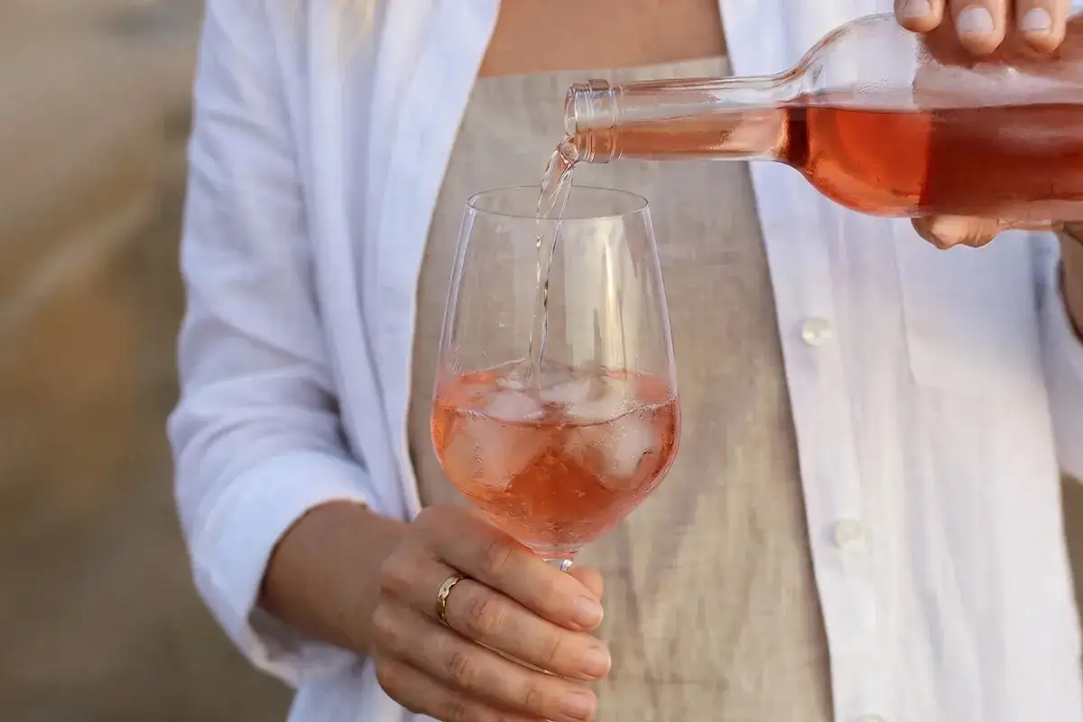 Eine Person gießt Roséwein mit Eiswürfeln in ein Glas. Die ideale Roséwein Temperatur für diesen erfrischenden Genuss.