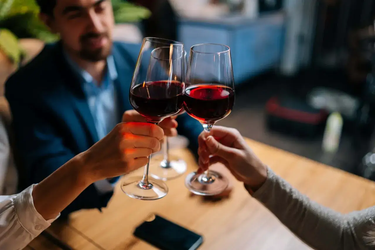 Drei Personen stoßen mit Rotwein an. Sie halten das weinglas richtig, am Stiel, um den Wein nicht zu erwärmen.