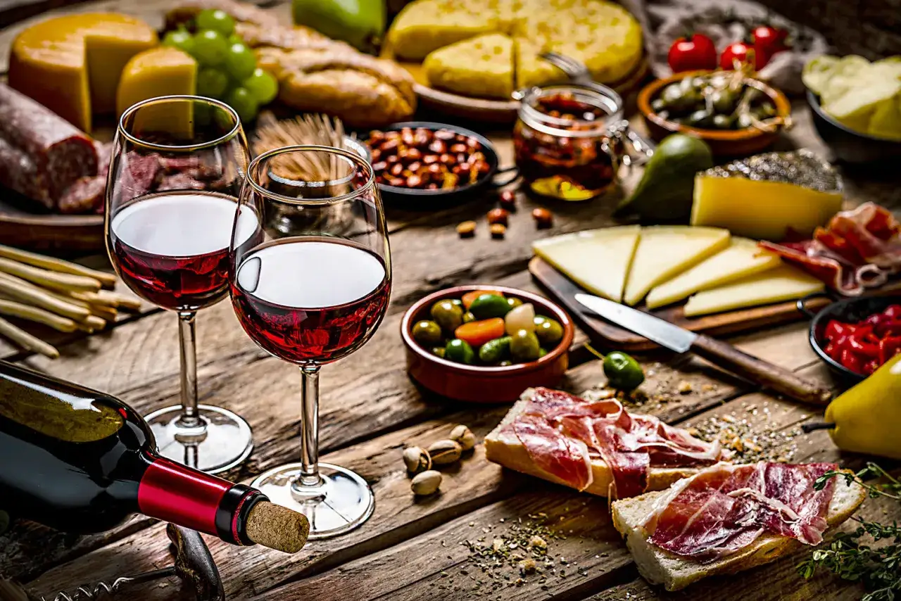 Zwei Gl&auml;ser Rotwein, ein Cabernet Franc, stehen neben einer Flasche und einer Auswahl an Tapas: K&auml;se, Schinken, Oliven und Brot.