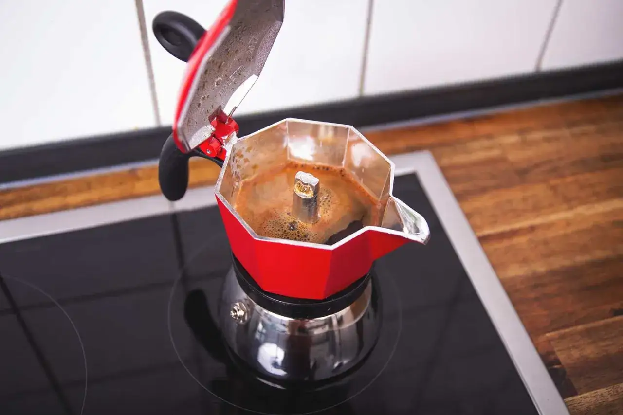 Rote Herdkanne mit frisch gebrühtem Kaffee auf einem Induktionskochfeld. Der Duft von Kaffee liegt in der Luft.