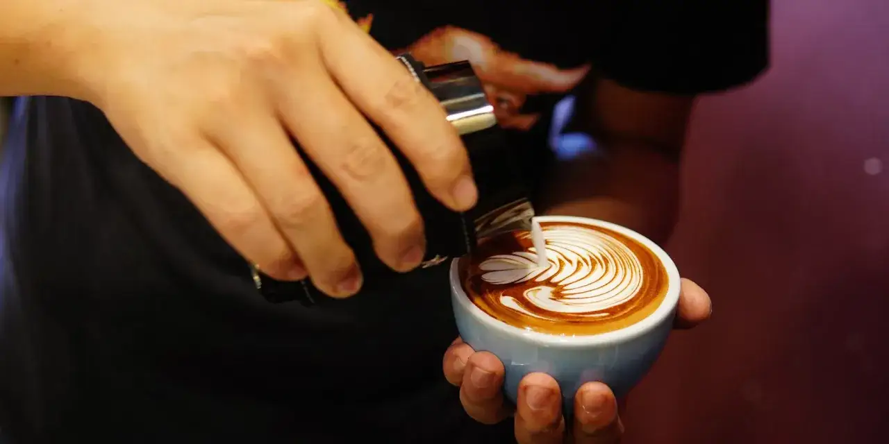 Barista art: Ein Barista gie&szlig;t Milch in einen Kaffee und kreiert ein sch&ouml;nes Muster.