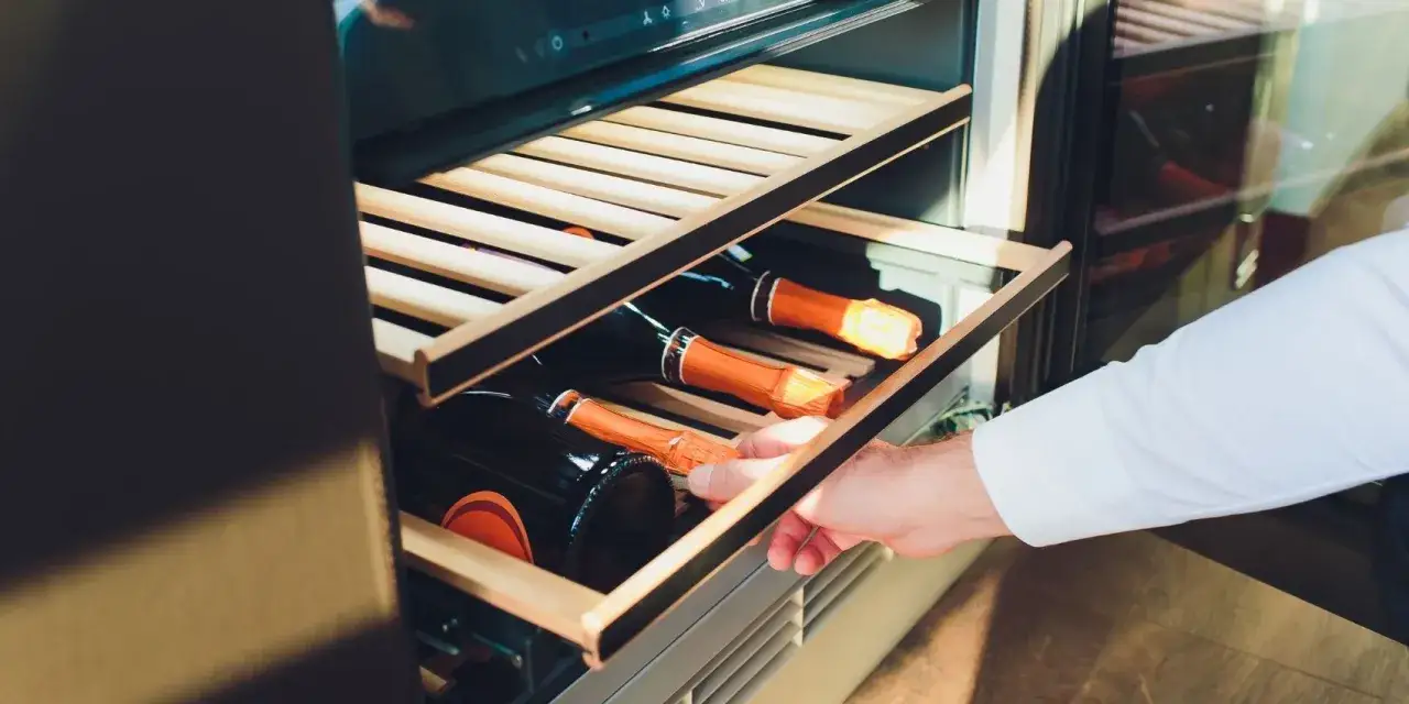 Mann öffnet Weinkühlschrank mit Rotweinflaschen. So bleibt Rotwein offen haltbar.