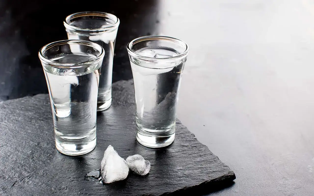 Drei Gläser mit eisgekühltem Wodka stehen auf einem dunklen Stein. Was ist Wodka? Ein klarer, starker Schnaps, perfekt für kalte Nächte.