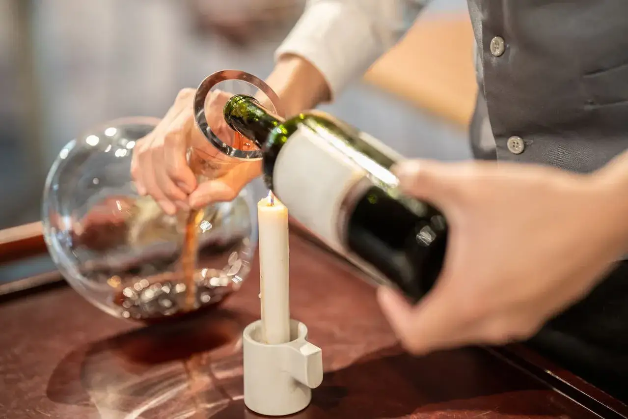 Wein wird mit Kerzenlicht dekantiert, um Ablagerungen zu erkennen. Ein Beispiel für sorgfältiges Dekantieren.